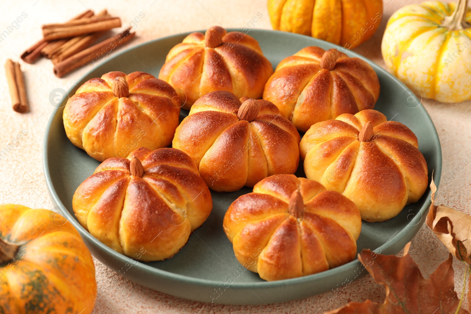 Photo of Tasty pumpkin shaped buns and ingredients on beige textured table