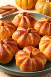 Photo of Tasty pumpkin shaped buns on beige table, closeup