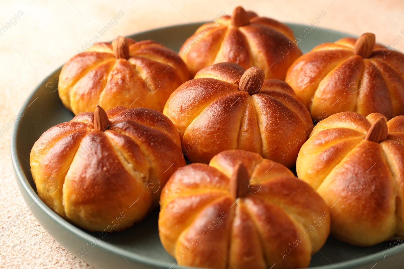 Photo of Tasty pumpkin shaped buns on beige textured table, closeup