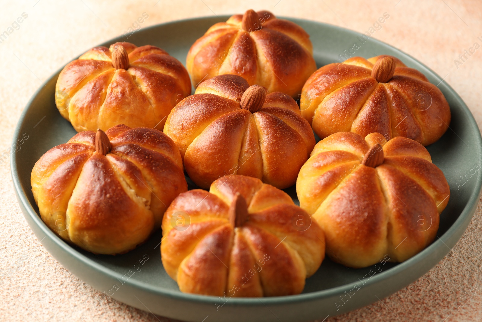 Photo of Tasty pumpkin shaped buns on beige textured table, closeup