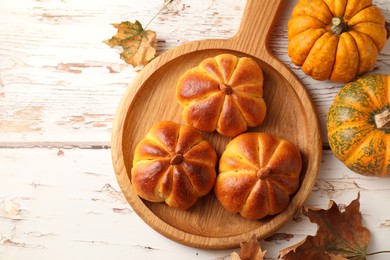 Photo of Tasty pumpkin shaped buns, ingredients and dry leaves on old wooden table, flat lay