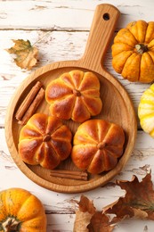 Photo of Tasty pumpkin shaped buns, ingredients and dry leaves on old wooden table, flat lay