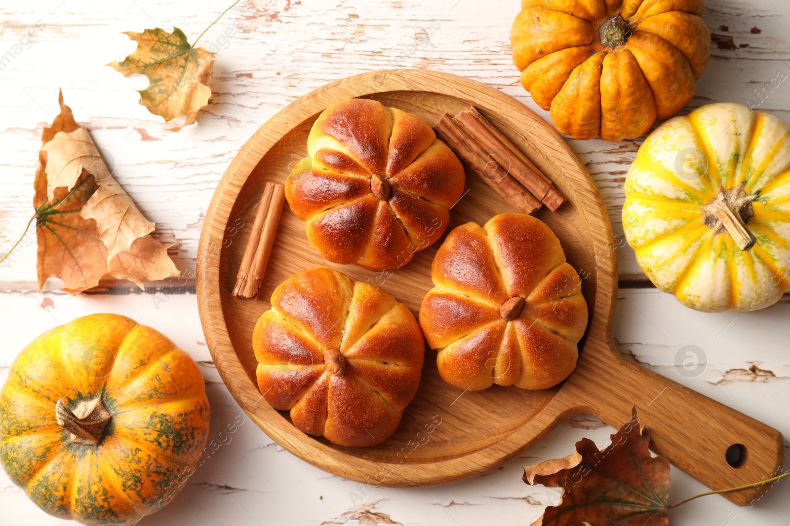 Photo of Tasty pumpkin shaped buns, ingredients and dry leaves on old wooden table, flat lay