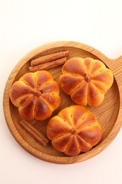 Photo of Tasty pumpkin shaped buns and cinnamon sticks on white table, top view