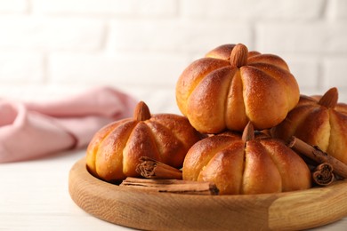 Photo of Tasty pumpkin shaped buns and cinnamon sticks on white table, closeup