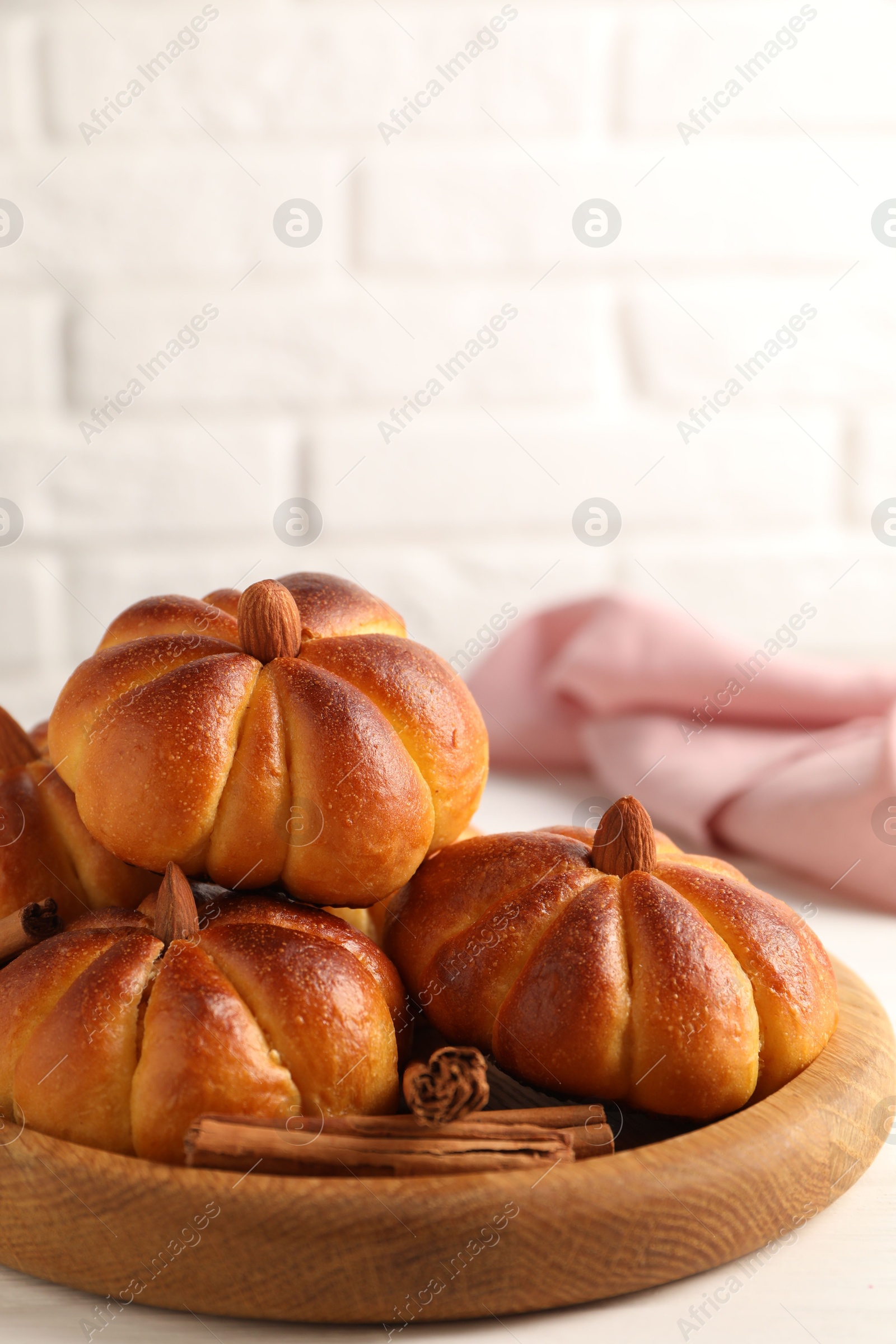 Photo of Tasty pumpkin shaped buns and cinnamon sticks on white table