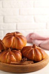 Photo of Tasty pumpkin shaped buns and cinnamon sticks on white table