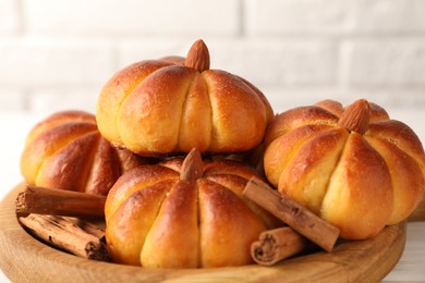 Photo of Tasty pumpkin shaped buns and cinnamon sticks on white table, closeup