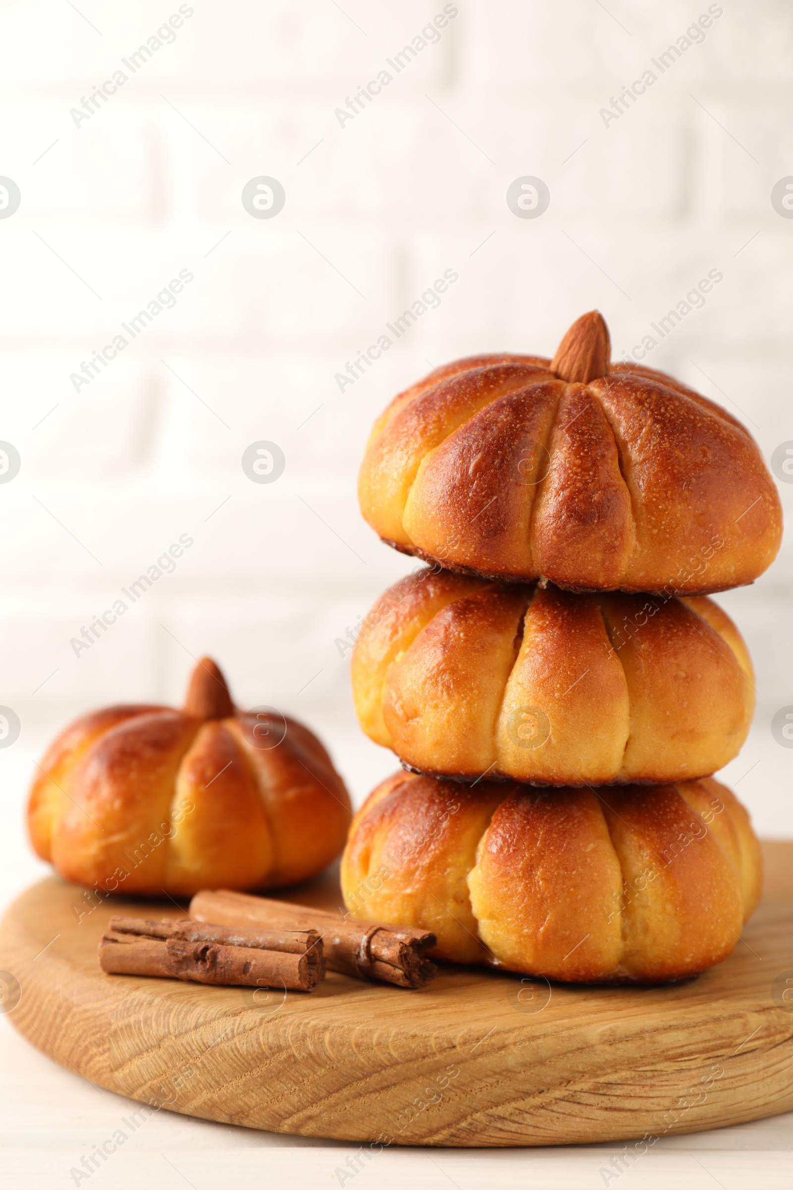 Photo of Tasty pumpkin shaped buns and cinnamon sticks on white table, closeup