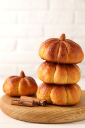 Photo of Tasty pumpkin shaped buns and cinnamon sticks on white table, closeup