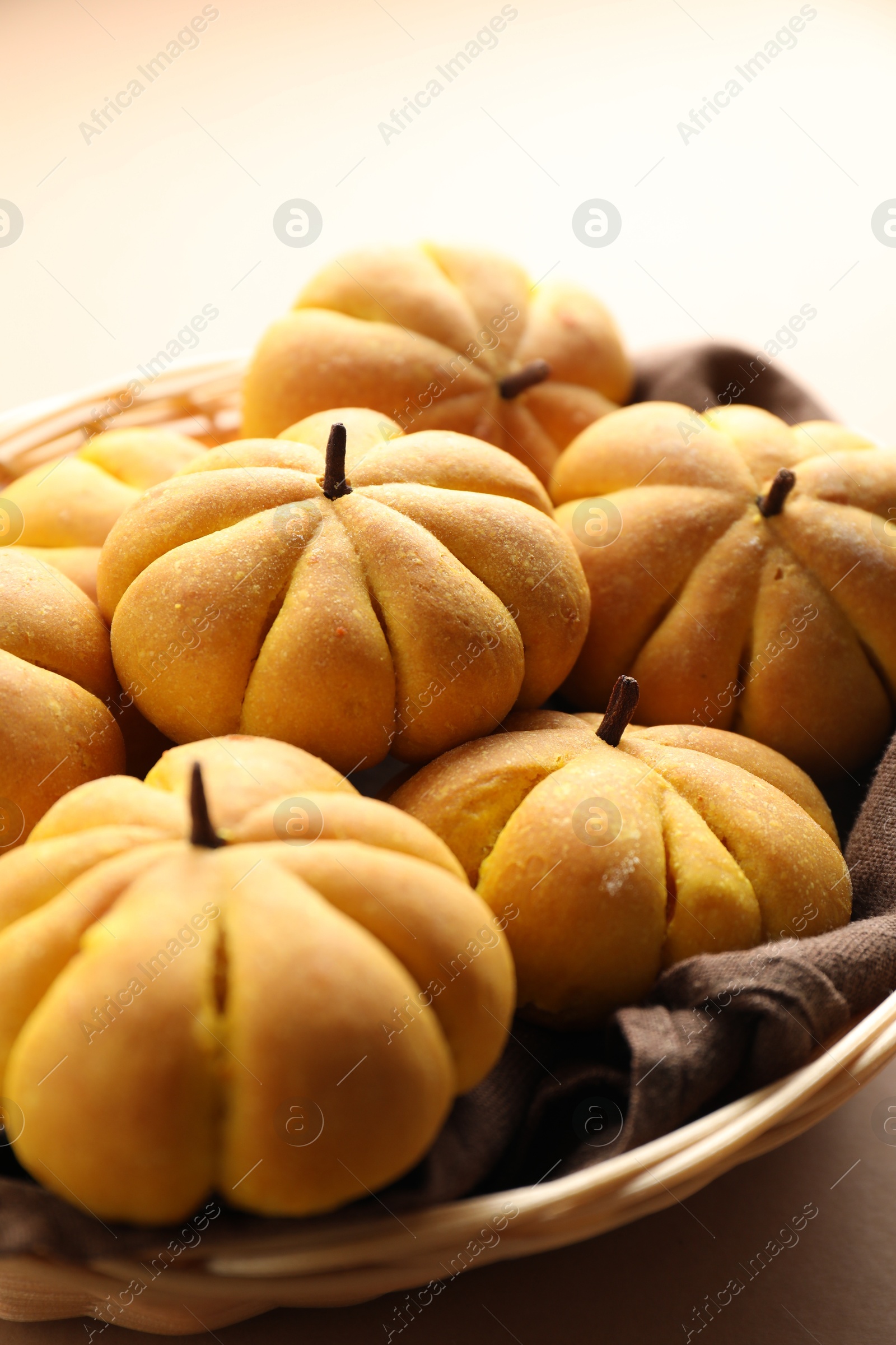 Photo of Wicker basket with tasty pumpkin shaped buns on beige background, closeup