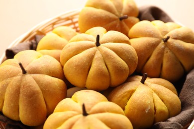 Photo of Wicker basket with tasty pumpkin shaped buns on beige background, closeup