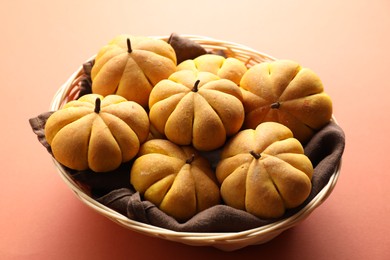 Photo of Wicker basket with tasty pumpkin shaped buns on light red background, closeup