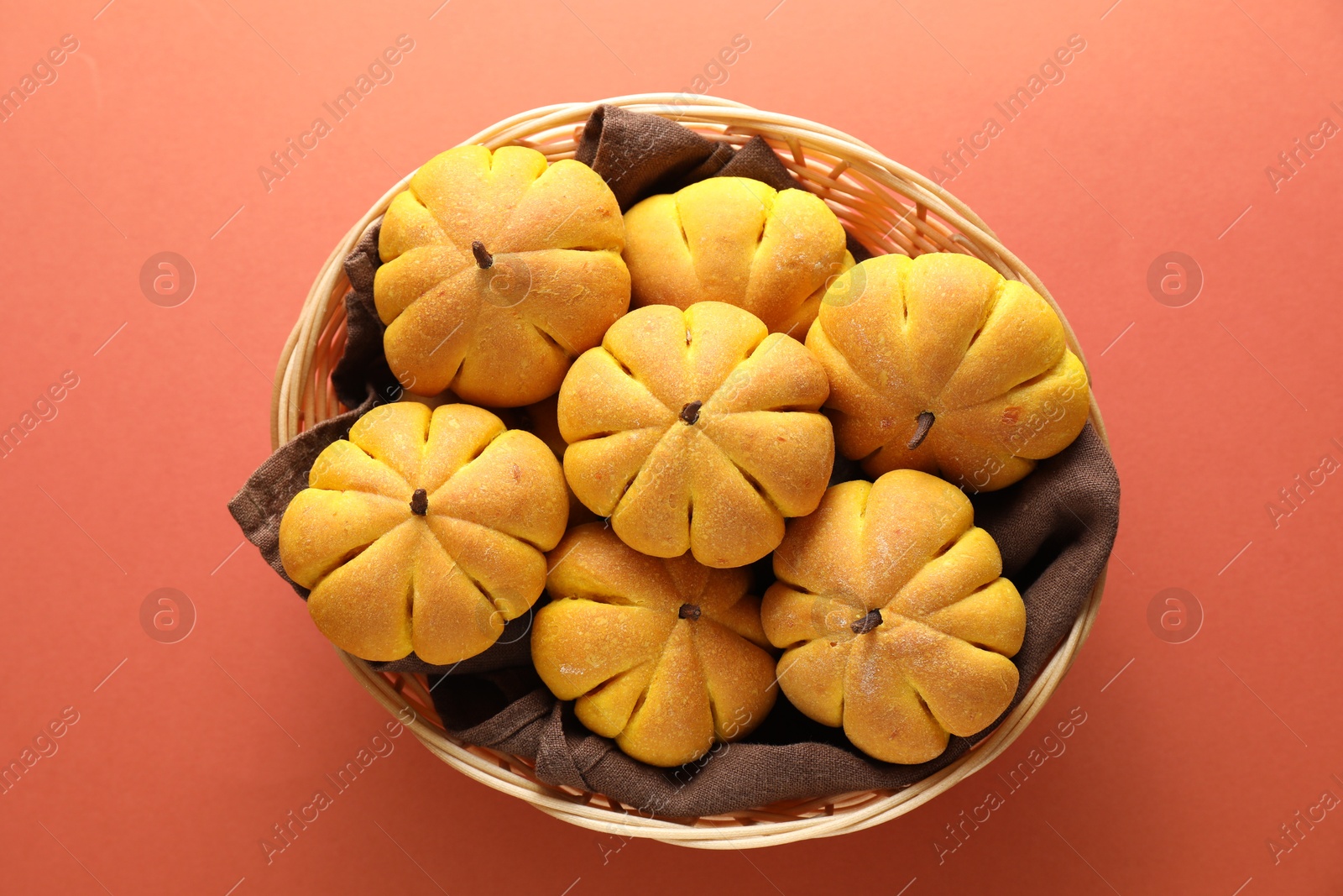 Photo of Wicker basket with tasty pumpkin shaped buns on light red background, top view