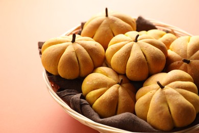 Photo of Wicker basket with tasty pumpkin shaped buns on light red background, closeup