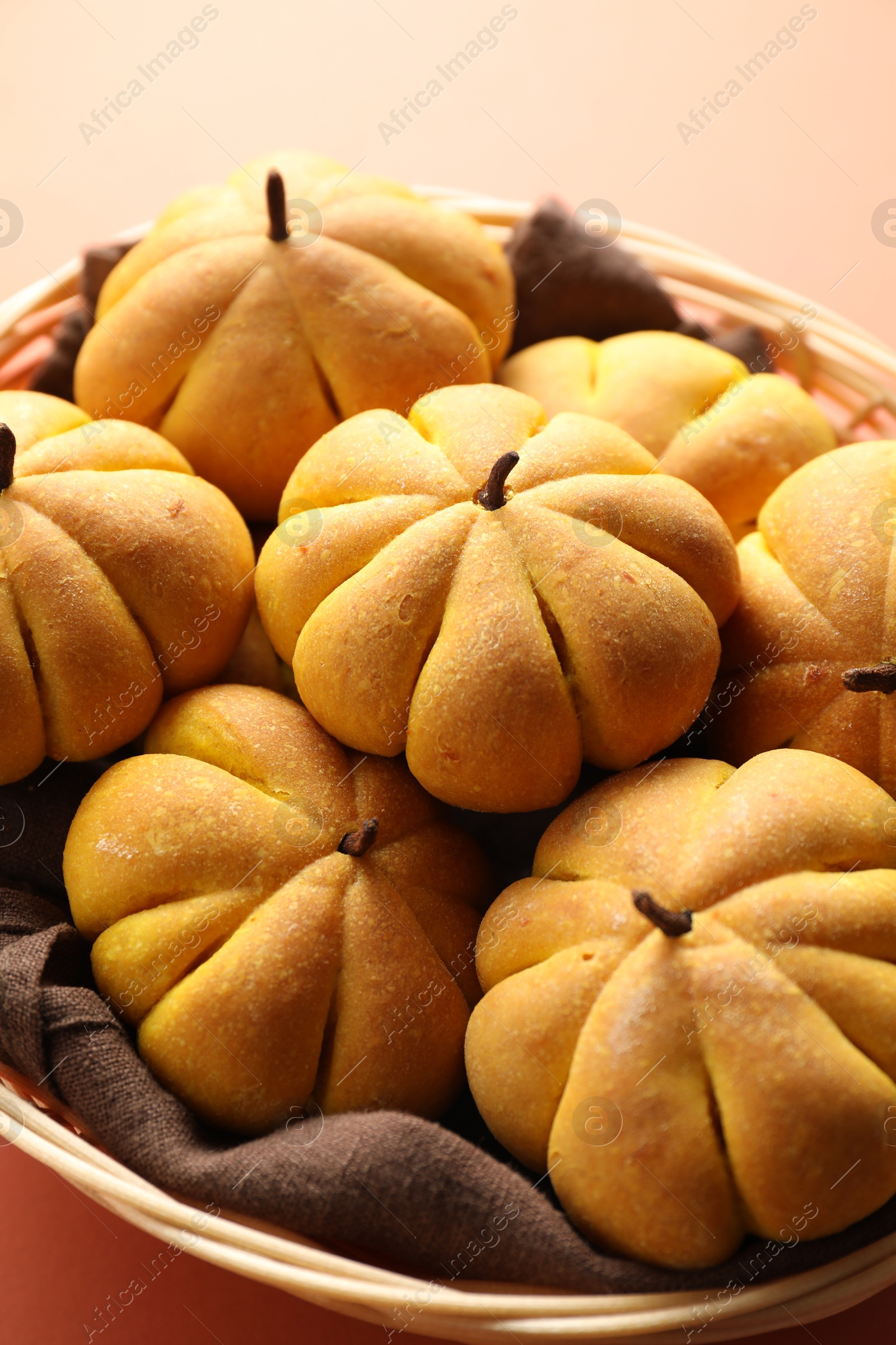 Photo of Wicker basket with tasty pumpkin shaped buns on light red background, closeup