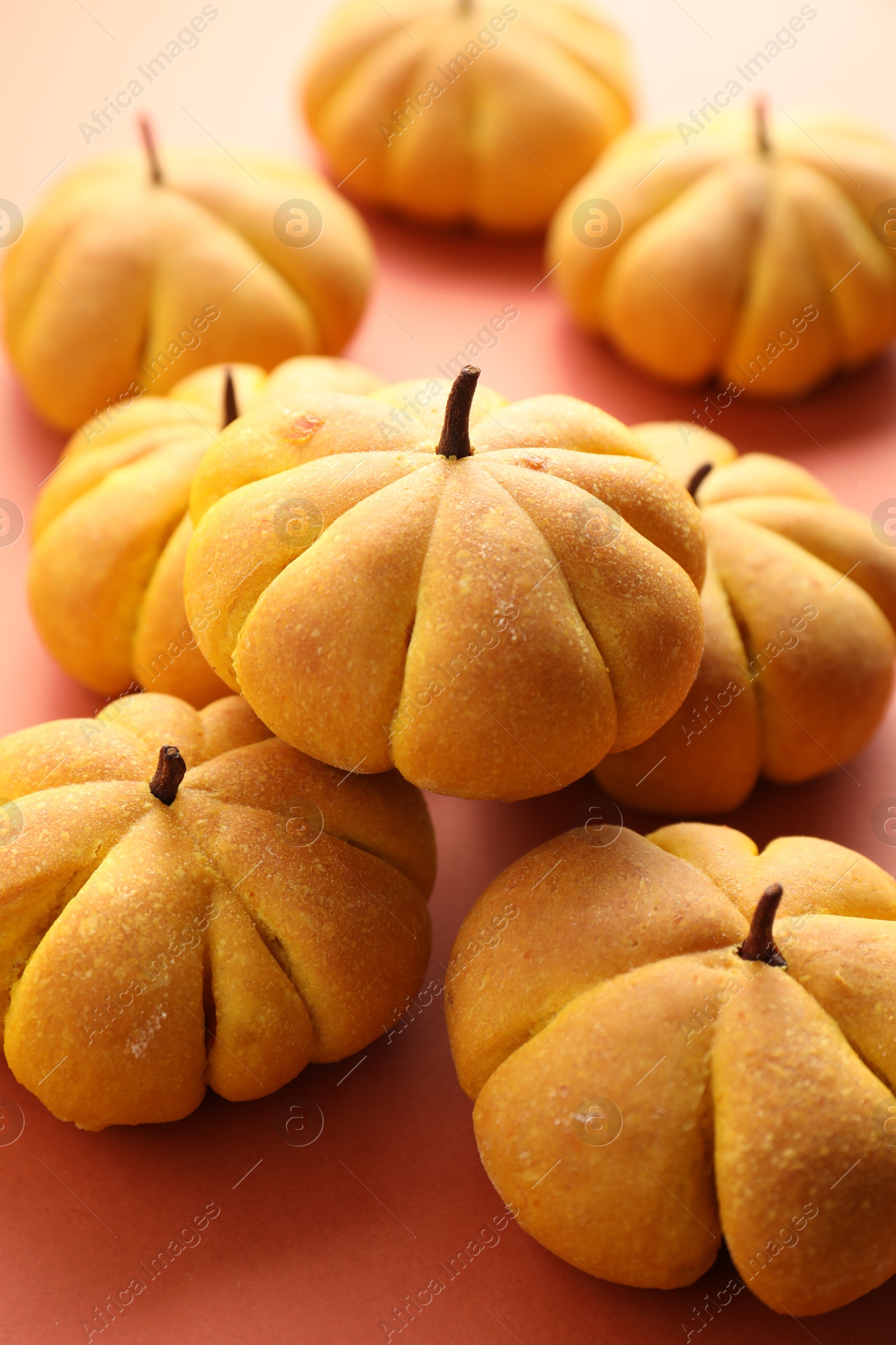 Photo of Pile of tasty pumpkin shaped buns on light red background, closeup