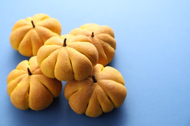 Photo of Pile of tasty pumpkin shaped buns on blue background, closeup. Space for text