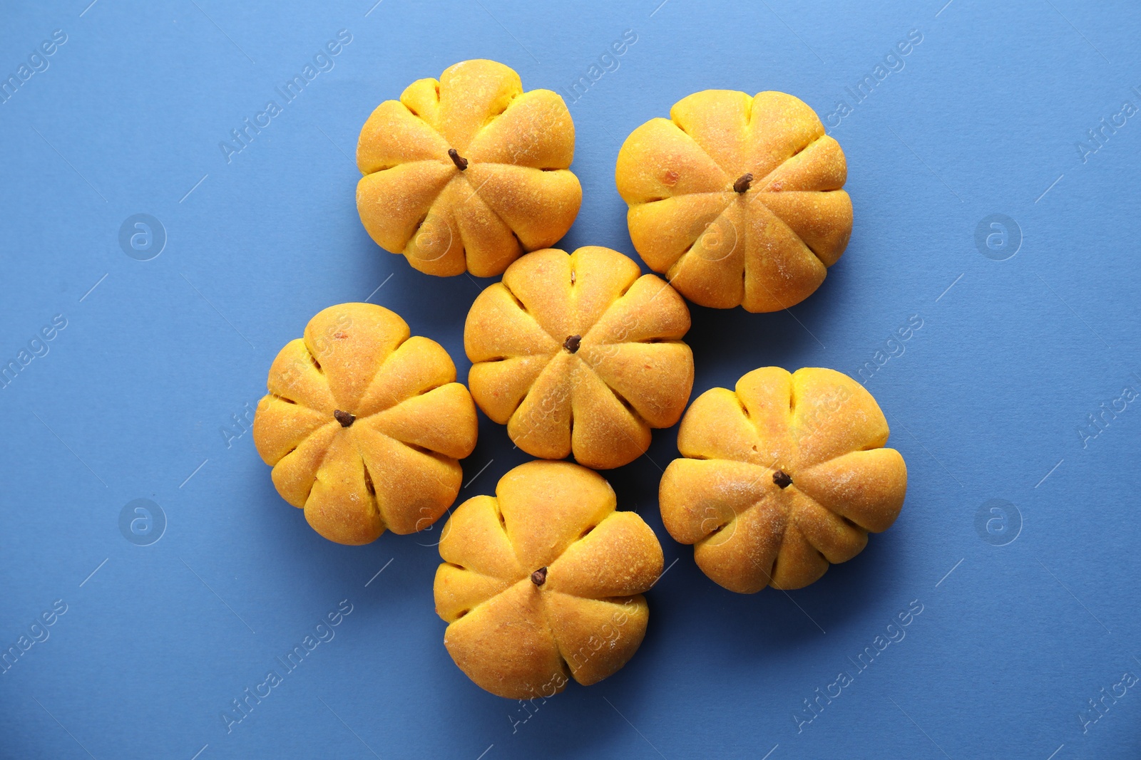 Photo of Pile of tasty pumpkin shaped buns on blue background, flat lay