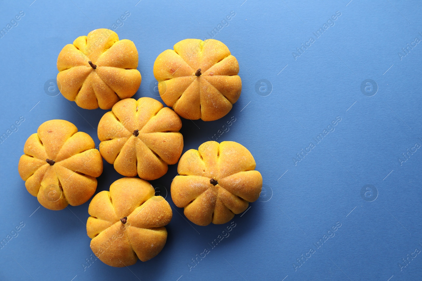 Photo of Pile of tasty pumpkin shaped buns on blue background, flat lay. Space for text