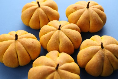 Photo of Pile of tasty pumpkin shaped buns on blue background, closeup