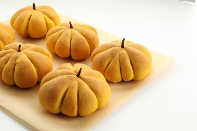 Photo of Parchment with tasty pumpkin shaped buns on white background, closeup