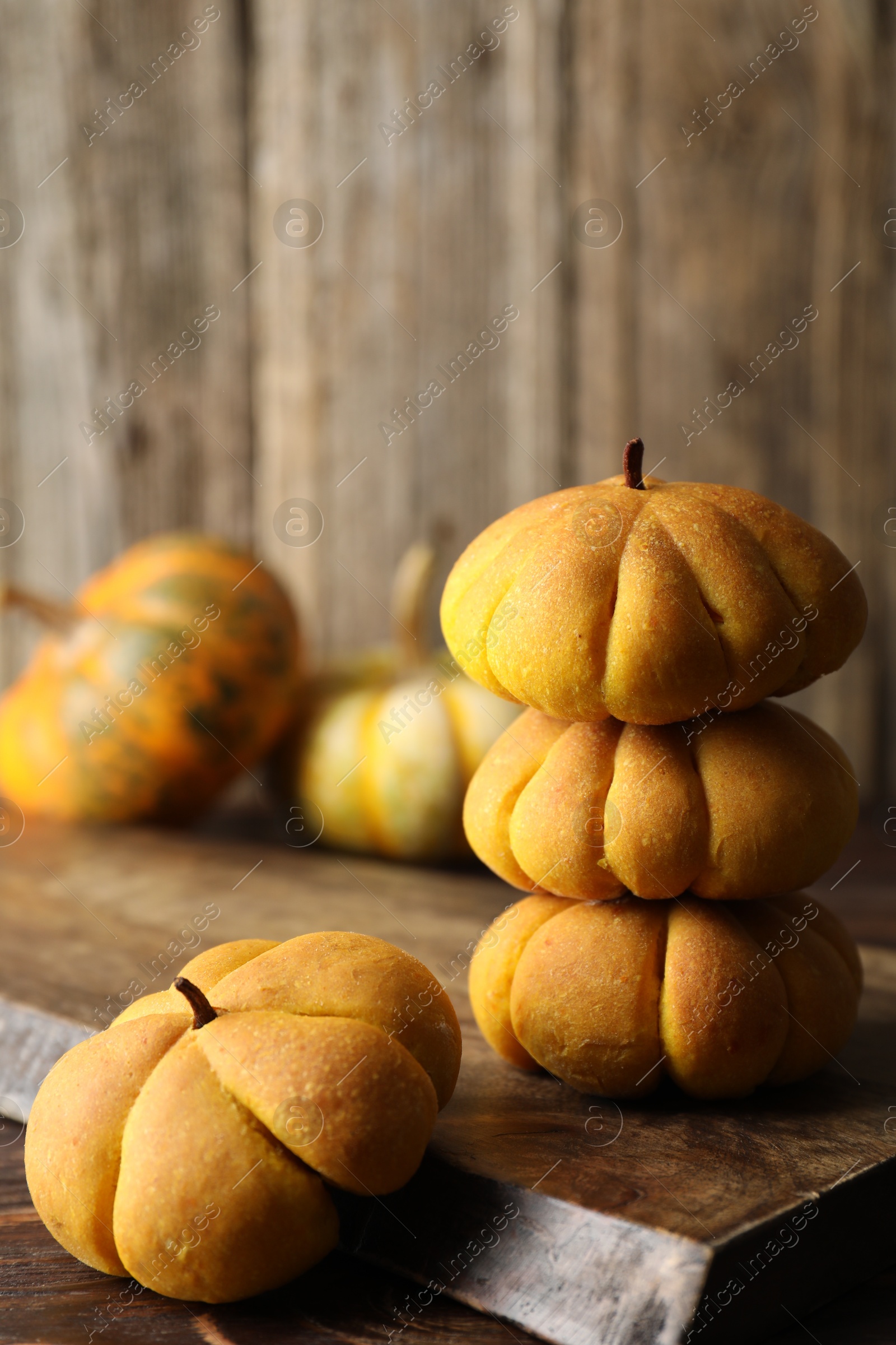 Photo of Tasty pumpkin shaped buns on wooden table, closeup