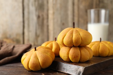 Photo of Tasty pumpkin shaped buns on wooden table, closeup