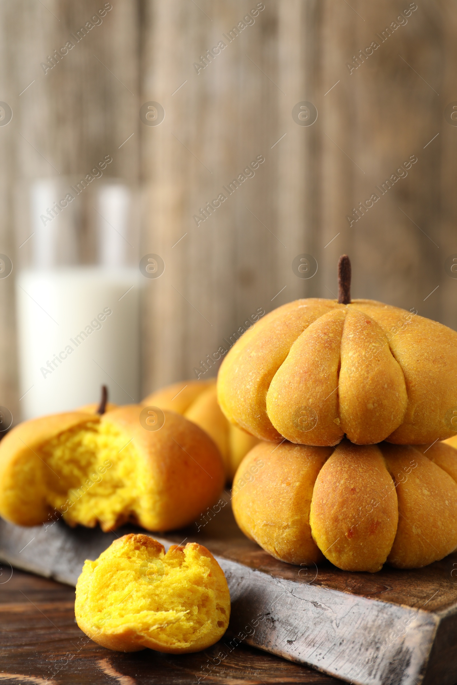 Photo of Tasty pumpkin shaped buns on wooden table, closeup