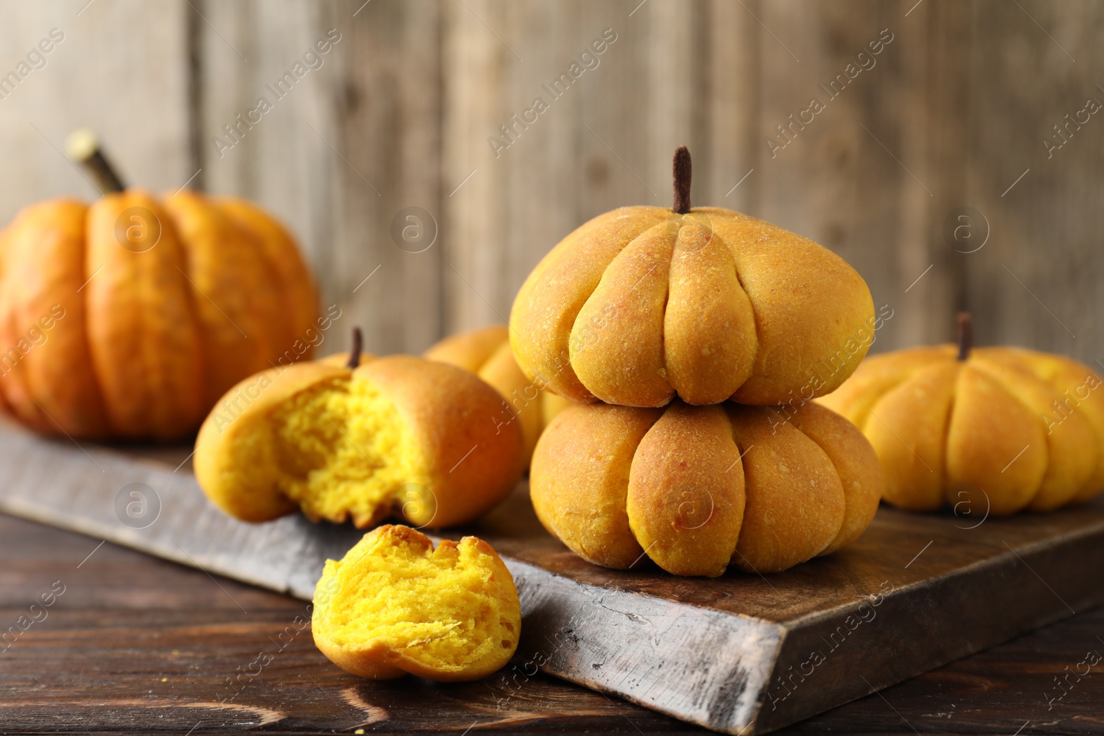 Photo of Tasty pumpkin shaped buns on wooden table, closeup