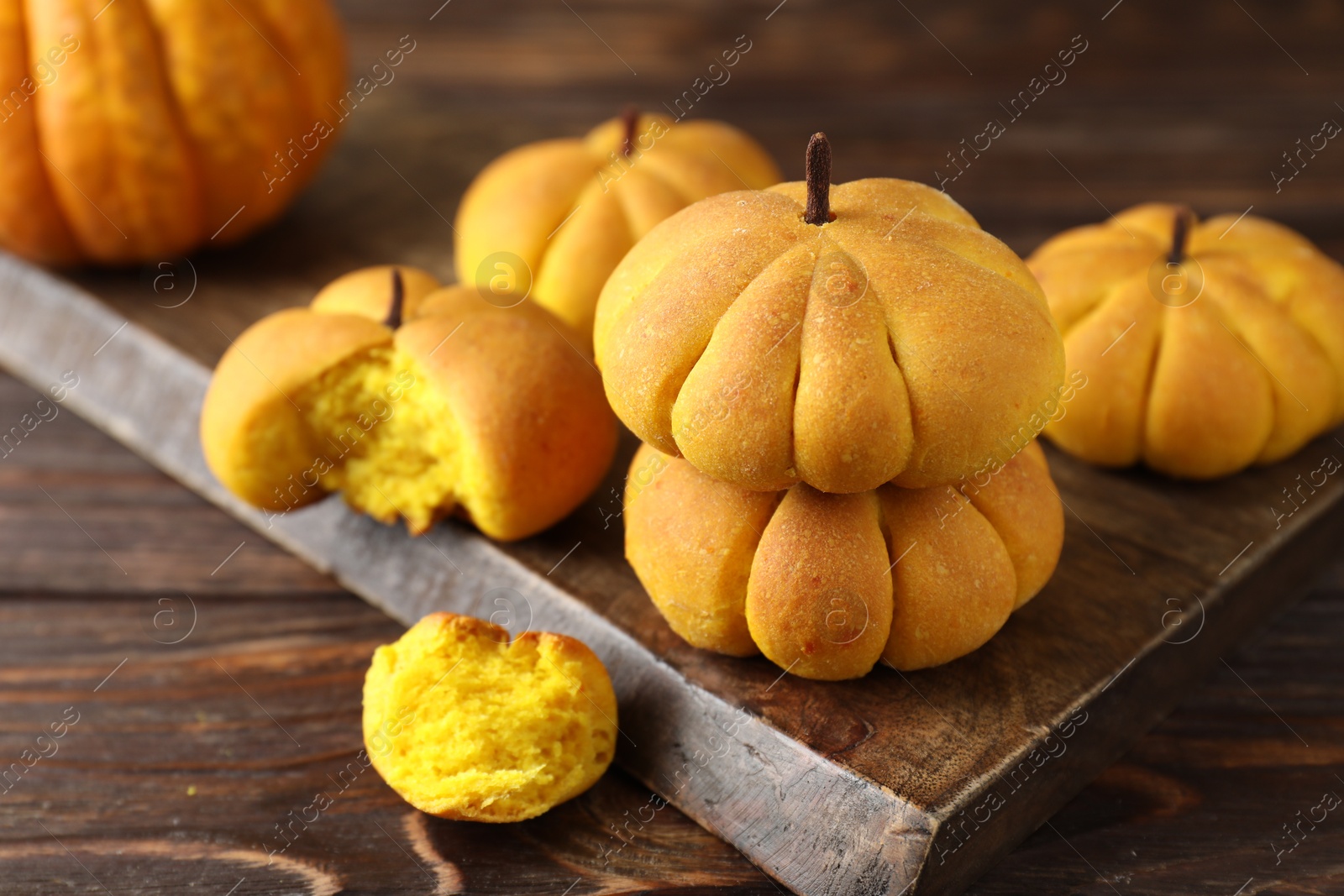 Photo of Tasty pumpkin shaped buns on wooden table, closeup