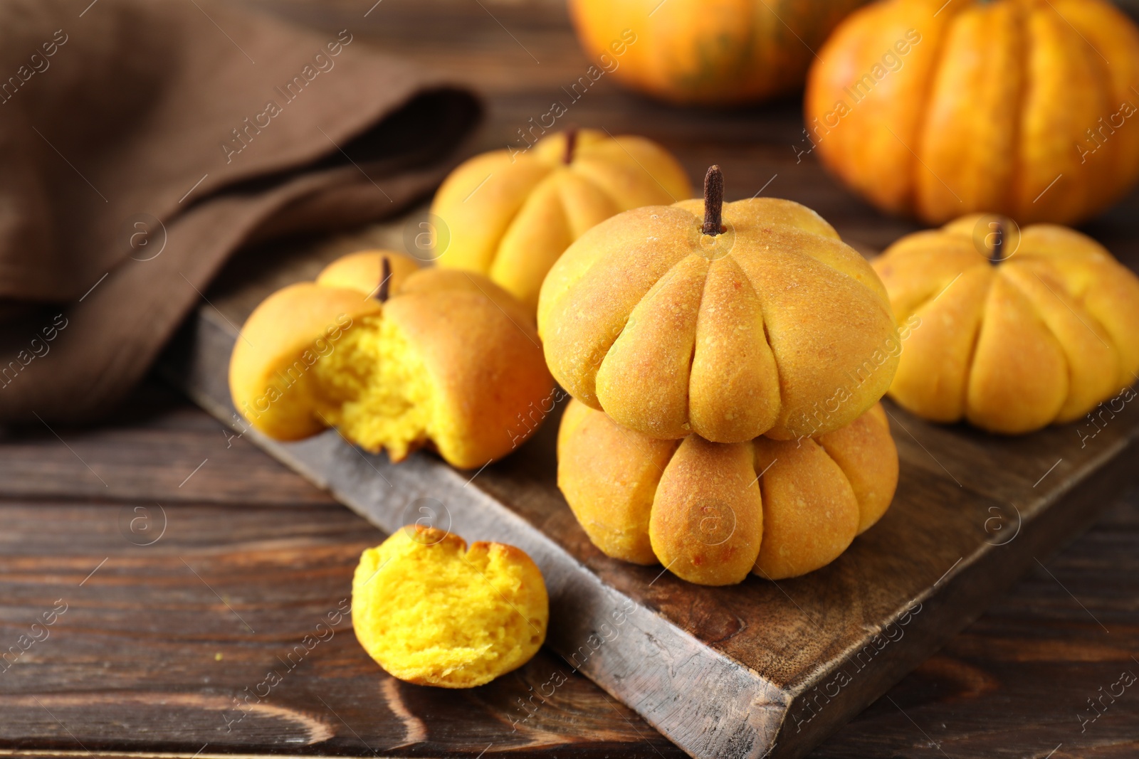 Photo of Tasty pumpkin shaped buns on wooden table, closeup