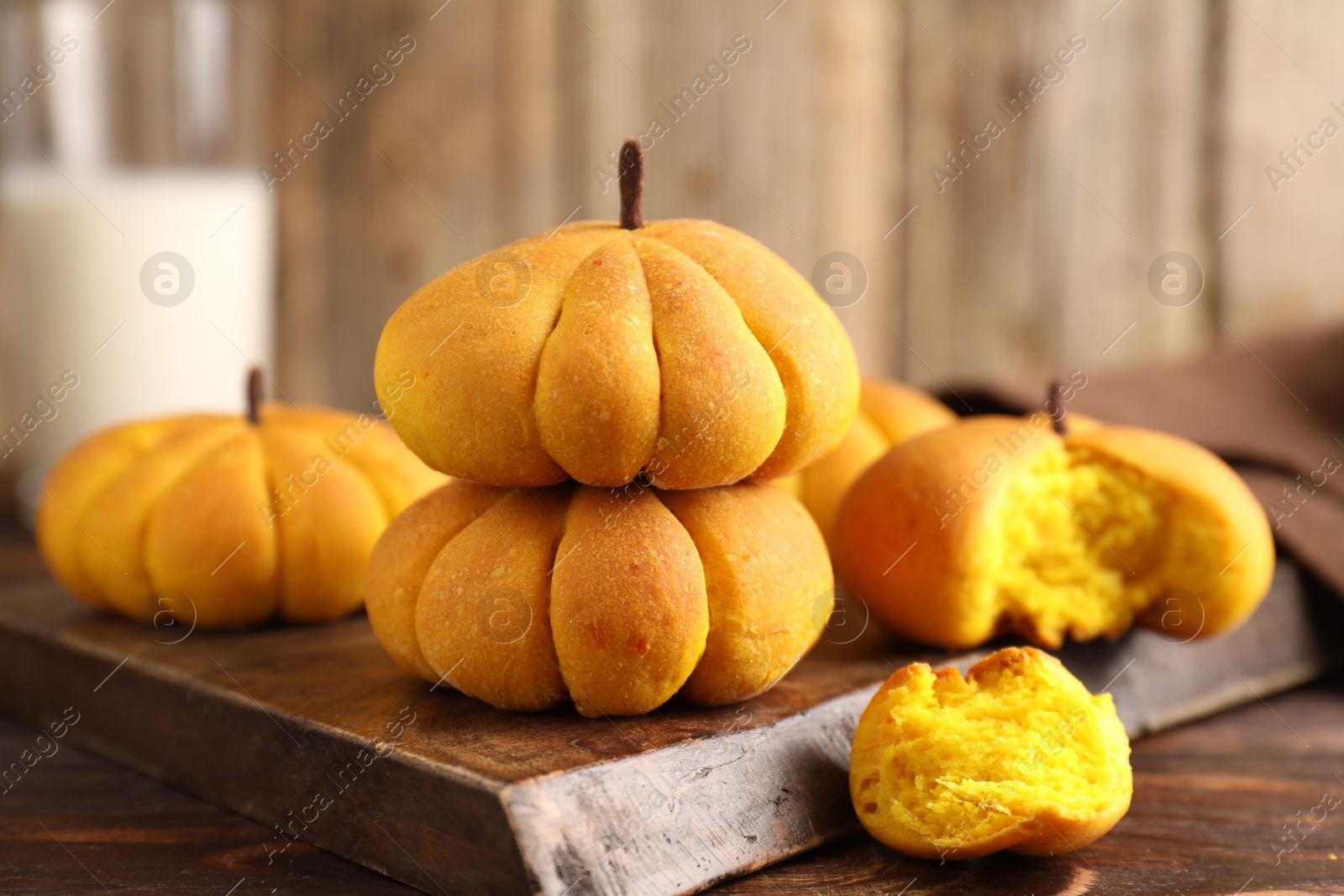 Photo of Tasty pumpkin shaped buns on wooden table, closeup