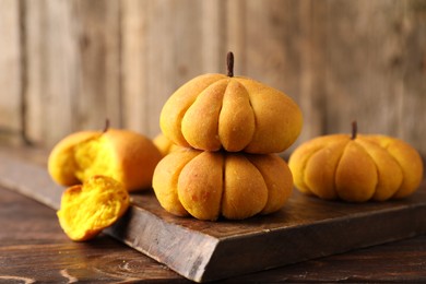 Photo of Tasty pumpkin shaped buns on wooden table, closeup