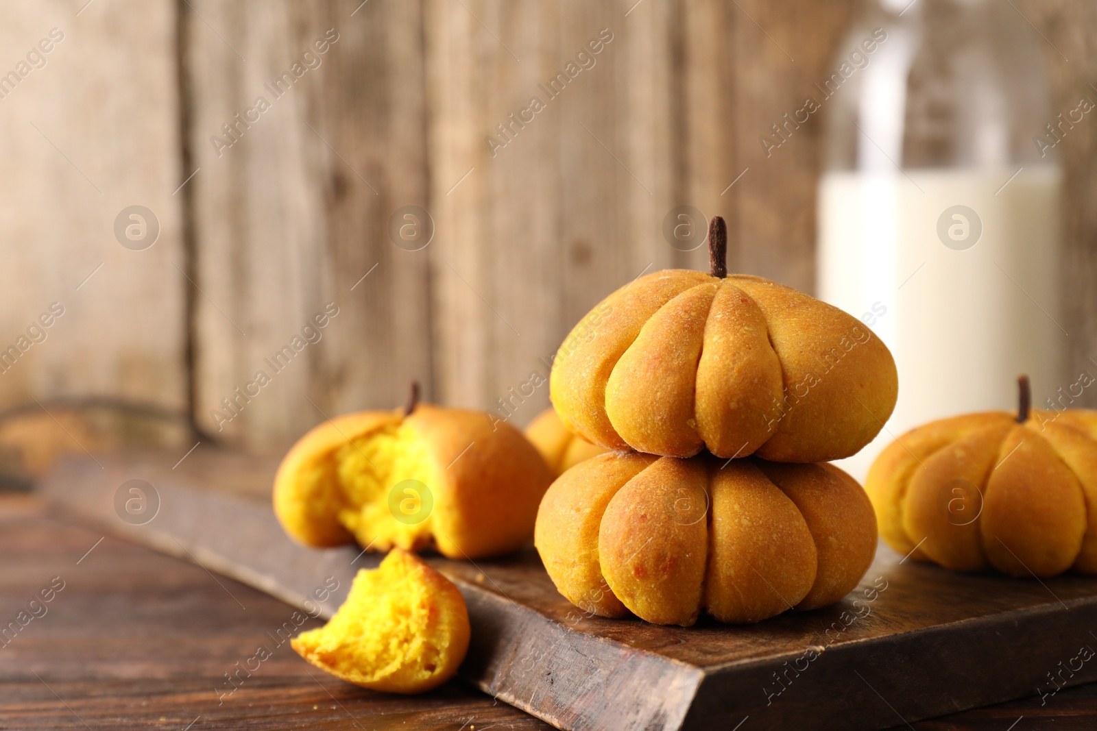 Photo of Tasty pumpkin shaped buns on wooden table, closeup. Space for text