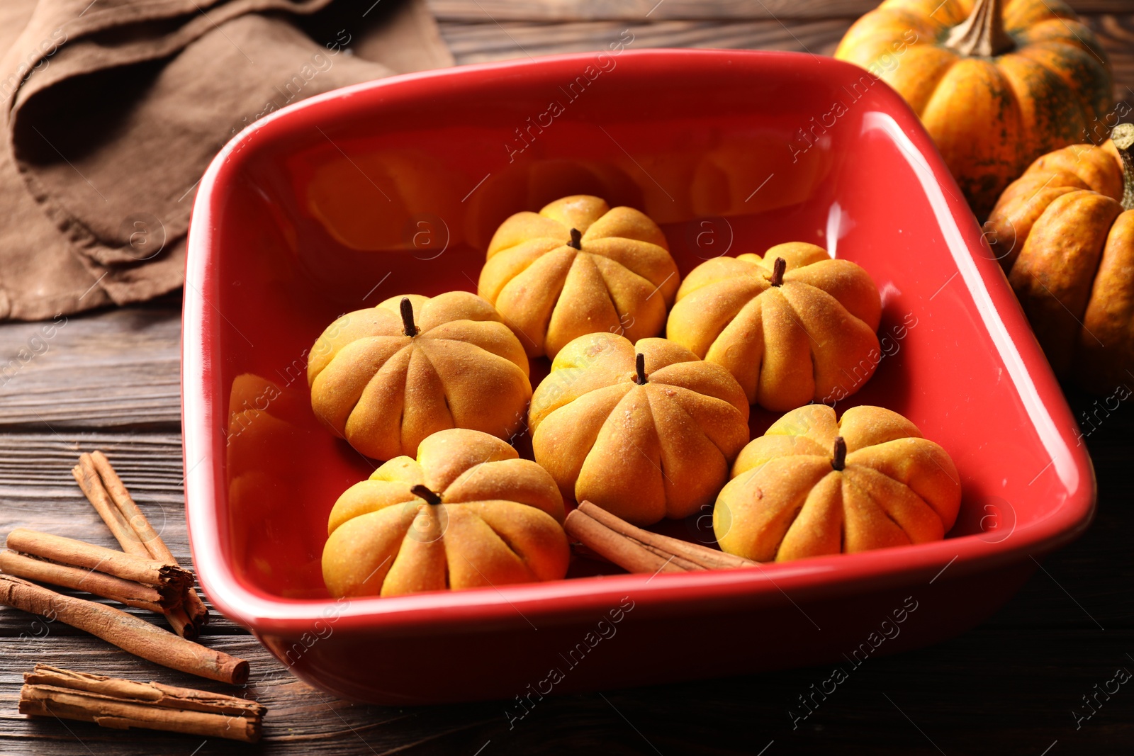 Photo of Baking tray with tasty pumpkin shaped buns and cinnamon sticks on wooden table, closeup