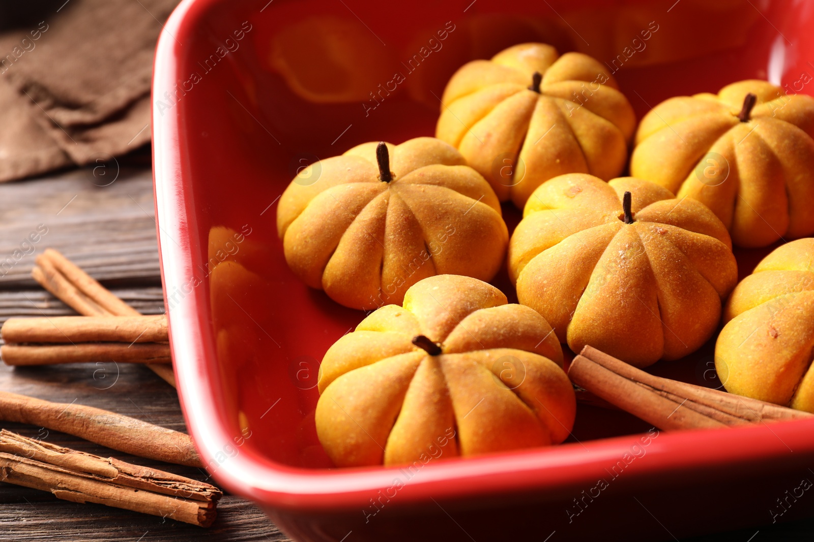 Photo of Baking tray with tasty pumpkin shaped buns and cinnamon sticks on wooden table, closeup