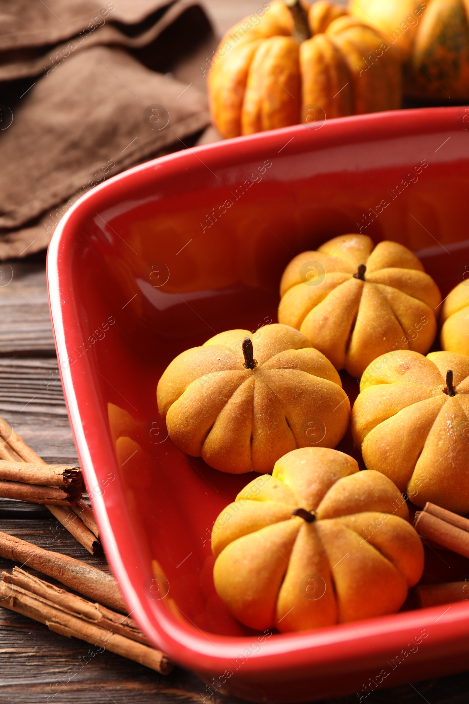 Photo of Baking tray with tasty pumpkin shaped buns and cinnamon sticks on wooden table, closeup