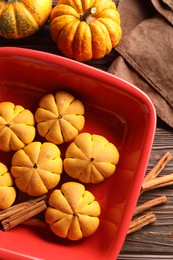 Photo of Baking tray with tasty pumpkin shaped buns and cinnamon sticks on wooden table, flat lay