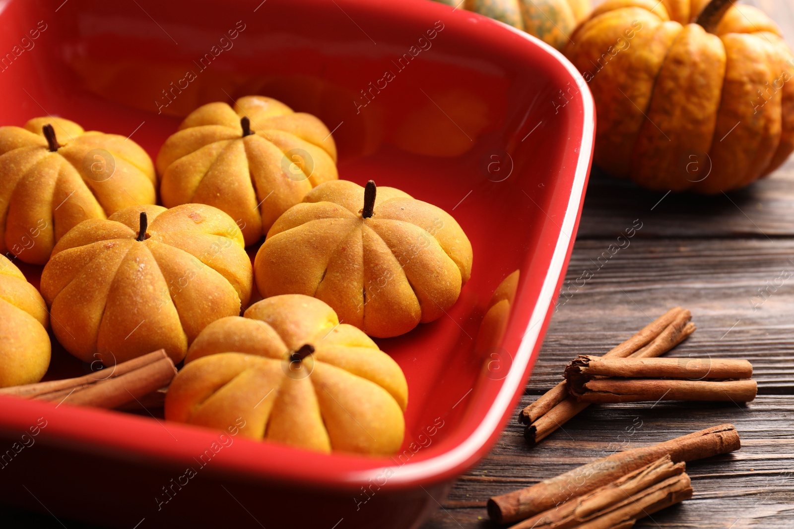 Photo of Baking tray with tasty pumpkin shaped buns and cinnamon sticks on wooden table, closeup