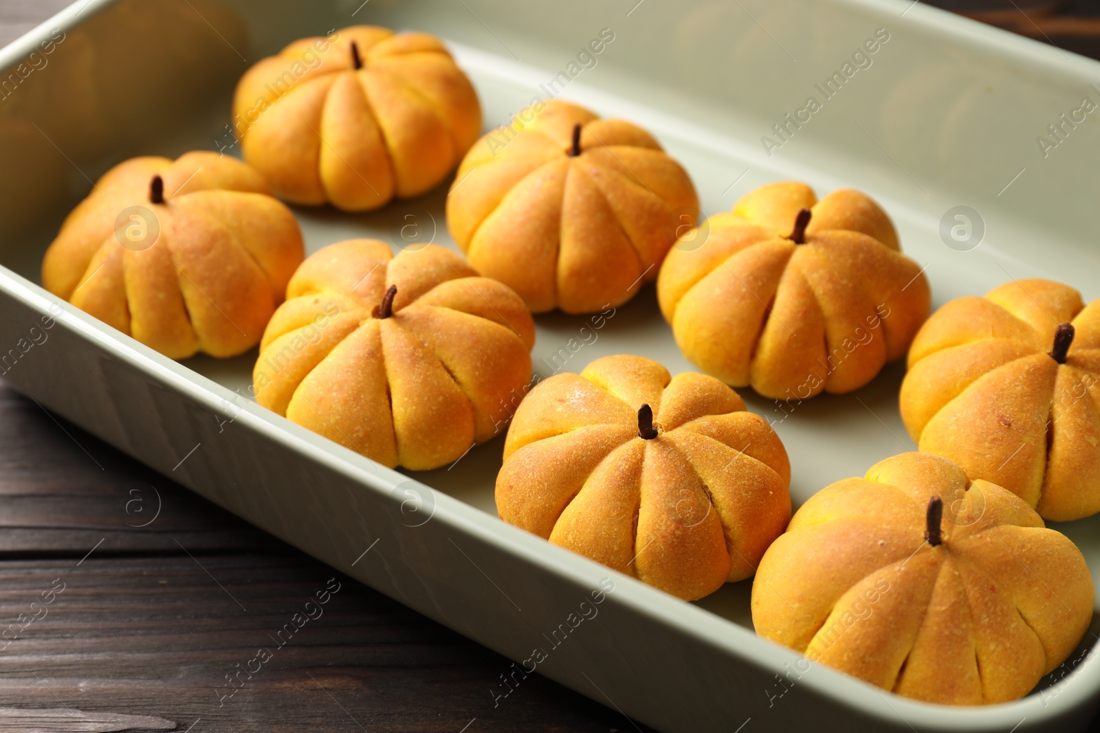 Photo of Baking tray with tasty pumpkin shaped buns on wooden table, closeup