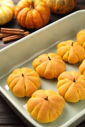 Photo of Baking tray with tasty pumpkin shaped buns on wooden table, closeup