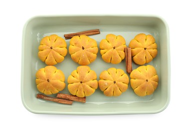 Photo of Baking tray with tasty pumpkin shaped buns and cinnamon sticks isolated on white, top view