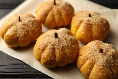 Parchment with tasty pumpkin shaped buns on wooden table, closeup