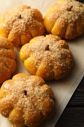 Photo of Parchment with tasty pumpkin shaped buns on wooden table, closeup