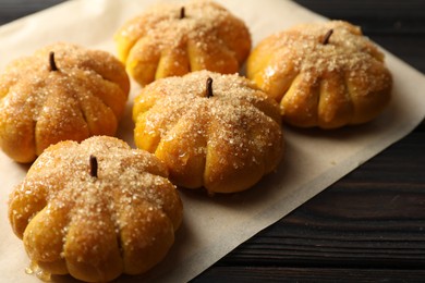 Photo of Parchment with tasty pumpkin shaped buns on wooden table, closeup