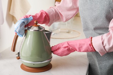 Woman wiping kettle with rag at countertop in kitchen, closeup