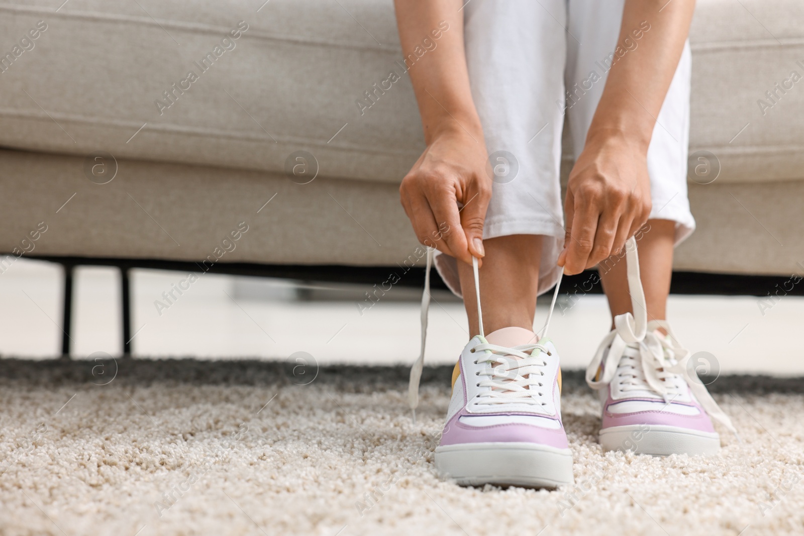 Photo of Woman tying shoelace of sneaker indoors, closeup. Space for text