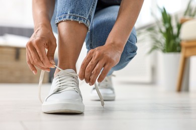 Photo of Woman tying shoelace of white sneaker indoors, closeup. Space for text