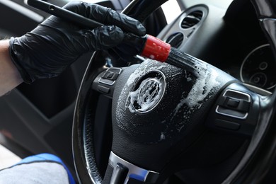 Man cleaning steering wheel with brush in car, closeup